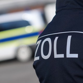 Ein Zoll-Mitarbeiter vor einem Polizeiwagen. In Worms ist dem Zoll nach eigenen Angaben ein Schlag gegen ein Schwarzarbeiter-Ring gelungen. 