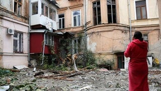 Nach einem russischen Luftangriff Mitte November in Odessa steht eine Frau in einem Bademantel vor stark zerstörten Wohnhäusern. 