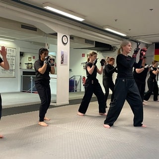 Mehrere Frauen in einem Trainingsraum üben die Selbstverteidigung.