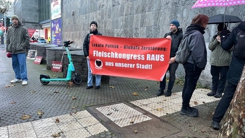 Protestierende halten ein Plakat mit der Aufschrift "Fleischkongress raus aus unserer Stadt".