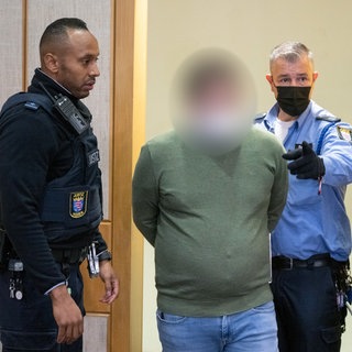 Mitarbeiter der Justiz führen den Angeklagten in den Verhandlungssaal des Landgerichts in Frankfurt. Der 35-jährige Angeklagte soll als Fußball-Jugendtrainer in zahlreichen Fällen Jugendliche vergewaltigt und missbraucht haben. (Foto aus dem Jahr 2022Erster Prozess) 