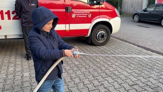 Ein Junge zielt bei der Bambini-Feuerwehr mit einem Wasserstrahl auf eine Flamme aus Papier. Mit dem Angebot wollen Feuerwehren Kinder früh für das Ehrenamt begeistern.