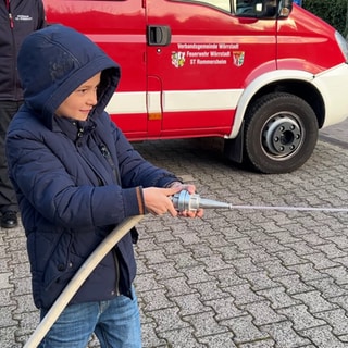 Ein Junge zielt bei der Bambini-Feuerwehr mit einem Wasserstrahl auf eine Flamme aus Papier. Mit dem Angebot wollen Feuerwehren Kinder früh für das Ehrenamt begeistern.