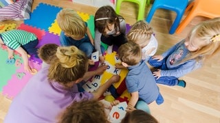 Eine Erzieherin kümmert sich um eine Gruppe von Kleinkindern. Wegen Haushalt – Stadt Mainz kann Kita-Erzieherinnen nicht hochstufen