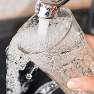 Eine Hand hält ein Glas unter einen Wasserhahn