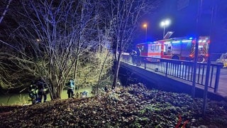 An einer Brücke über die Selz stehen ein Feuerwehr- und ein Notarztwagen, während Feuerwehrleute am Ufer stehen.