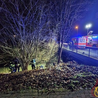 An einer Brücke über die Selz stehen ein Feuerwehr- und ein Notarztwagen, während Feuerwehrleute am Ufer stehen.