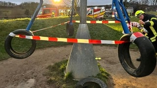 Ein Feuerwehrmann sichert ein Spielgerät aus Autoreifen mit Flatterband ab.