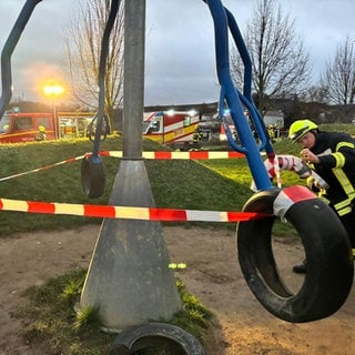 Ein Feuerwehrmann sichert ein Spielgerät aus Autoreifen mit Flatterband ab.