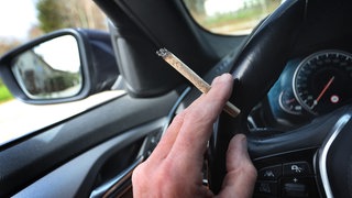 Ein Autofahrer hält einen Marihuana-Joint in der Hand.