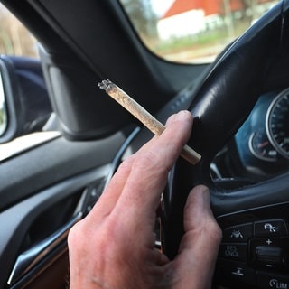 Ein Autofahrer hält einen Marihuana-Joint in der Hand.