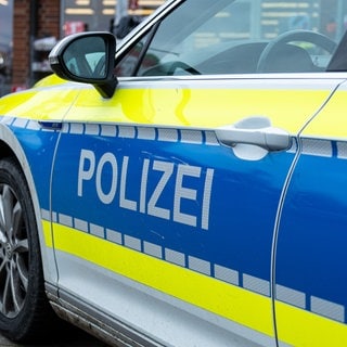 Im Vordergrund die Fahrertür eines Polizeiautos mit dem großen Schriftzug "Polizei", im Hintergrund ein Geschäft. (Sujetbild)