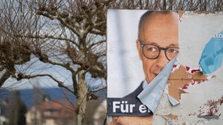 Ein beschädigtes Wahlplakat mit dem Foto von Kanzlerkandidat Friedrich Merz (CDU) für die Bundestagswahl 2025 steht am Rheinufer in Mainz.