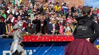 Vor dem Mainzer Staatstheater führt der Rosenmontagszug an der Tribüne mit prominenten Besuchern und Besucherinnen vorbei.