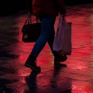Frau läuft im Dunkeln mit Einkaufstaschen durch eine Fußgängerzone