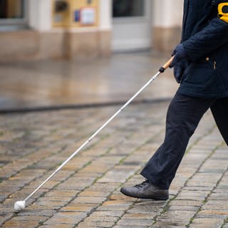 Eine blinde Person geht mit ihrem Blindenstock eine Straße entlang.