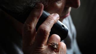 Polizei Trier warnt vor Schockanrufen . Seniorin hält einen Telefonhörer in der Hand 