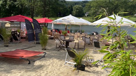 Stühle und Tische stehen unter Sonnenschirmen und Palmen im Sandstrand. Die Beachbar in Minden lädt nach dem Hochwasser 2021 wieder zum erholen ein.