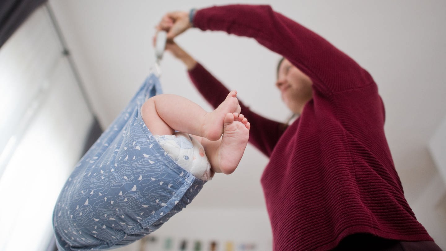 Eine Hebamme wiegt im Rahmen der Nachsorge ein Baby.
