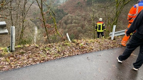 Feuerwehrleute stehen vor einer durchbrochenen Leitplanke an einem Steilhang bei Beuren, den ein Lkw hinabgestürzt ist.