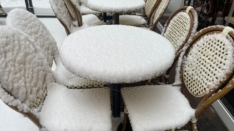 Verschneite Tische und Stühlle vor einem Cafe am Hauptmarkt in Trier. 