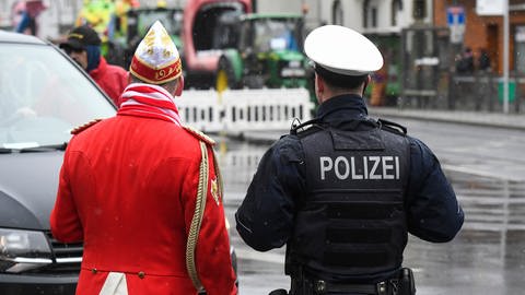 Ein Polizist steht neben einem Jecken auf der Straße. Wer sich beispielsweise als Polizist verkleiden möchte, sollte darauf achten, dass es nicht wie eine echte Uniform aussieht.
