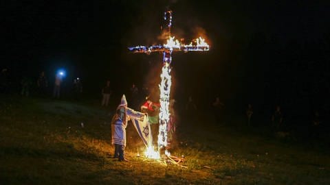 Das brennende Kreuz symbolisiert in der Ideologie des radikal-protestantischen Ku-Kluk-Klans das Licht Jesu-Christi. Solche Kreuze haben Mitglieder zum Beispiel auch als Drohung in den Vorgärten ihrer Gegner entzündet. 