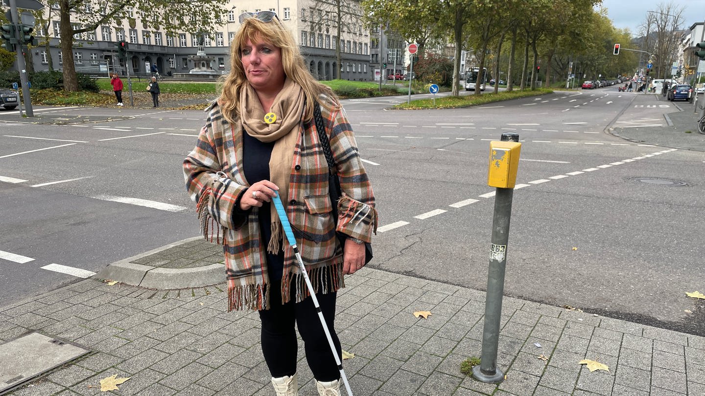Frau mit Blindenstock steht auf Fußgängerweg an defektem Ampelsignal.