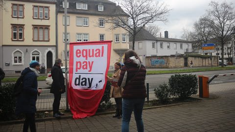 Der Landrat des Kreises Trier-Saarburg, Stefan Metzdorf (SPD, links), und die Gleichstellungsbeauftragte des Kreises, Angelika Mohr (rechts), hissen die Flagge zum Equal Pay Day.