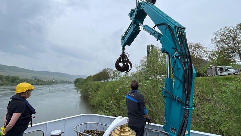 Der Kran am Bug der "Max Prüss" hebt Gestein am Rande der Mosel aus dem Wasser.