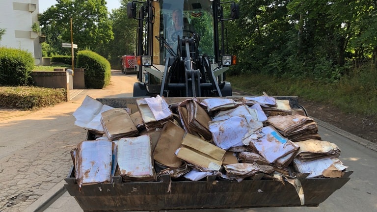 Ein Bagger transportiert vor dem Krankenhaus in Trier-Ehrang aufgeweichte Akten ab, die die Flut zerstört hat