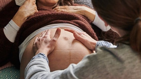 Eine Hebamme tastet den Bauch einer schwangeren Frau ab.