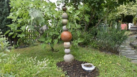 Upcycling im Garten: Eine alte Suppenschüssel mit Steinen darin dient als Tränke für Tiere. Auf einem Metallstab aufgereiht macht das Sammelsurium von unterschiedlichen Kugeln eine gute Figur.