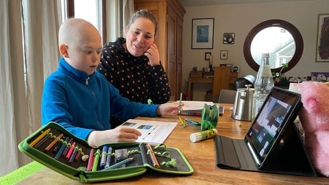 Bela macht Hausaufgaben mit Hilfe seiner Lehrerin und seiner Mutter.