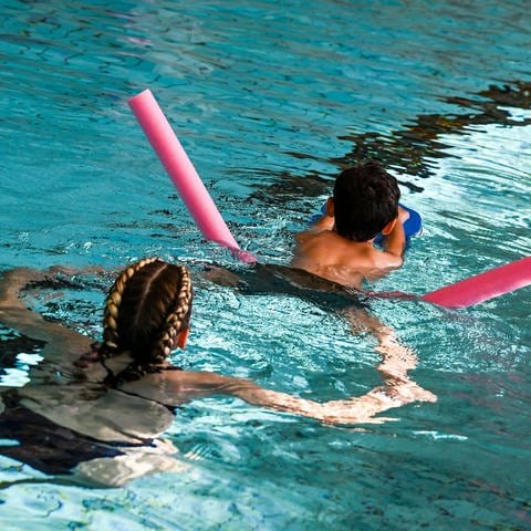 Ein Kind erhält Schwimmunterricht in einem Schwimmbad  In der Region Trier müssen Kinder teils ein Jahr lang auf einen Schwimmkurs warten.