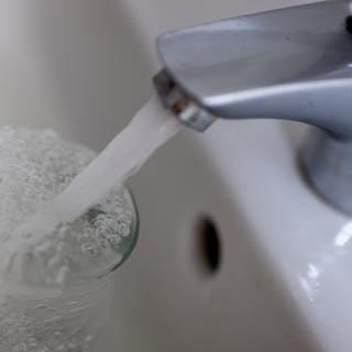 Tinkwasser läuft aus dem Wasserhahn im Badezimmer in ein Glas.