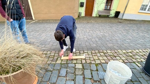 Raffer Jonas Thieltges legt sandgefüllte Plastikeier im Abstand einer preußischen Elle bereit. Bei der richtigen Eierlage rafft er echte, rohe Eier, die auf Sägespänen liegen.