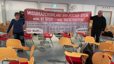 Vertreter von MissBit halten bei der Vorstellung der Missbrauchsstudie in Trier ein Plakat in die Luft: Aufschrift: Missbrauchsbilanz Ära Bischof Stein: Mind. 81 Täter! Mind. 340 Betroffene - Sie fordern außerdem Bischof Ackermann zum Rücktritt auf