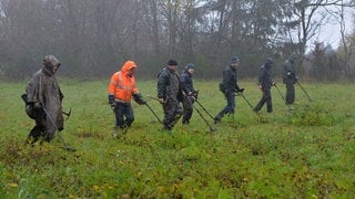 Männer mit Metallsuchgeräten durchsuchen die Wiese bei Riol nach antiken Fundstücken.