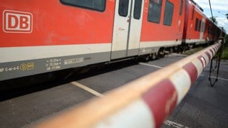 Ein Zug fährt über einen Bahnübergang, an dem die Schranke geschlossen ist.