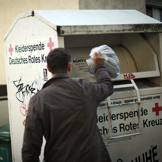 Mann wirft Kleider in Altkleidercontainer