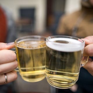 Weihnachtsmarktgäste stoßen mit zwei Gläsern mit weißem Glühwein an.