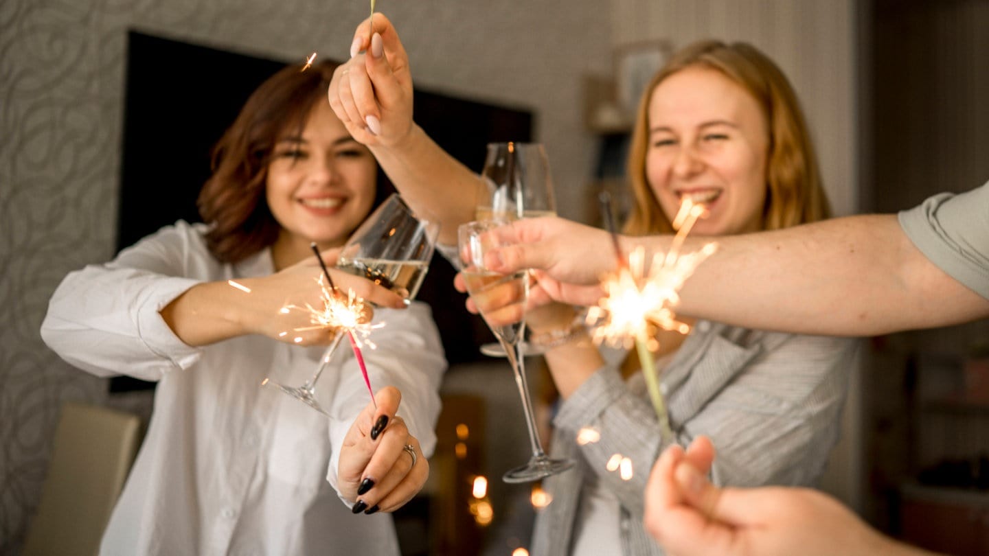 Fröhliche Menschen feiern Silvester mit Wunderkerzen und Sekt.