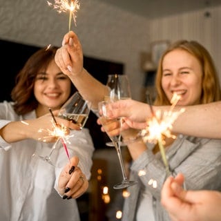 Fröhliche Menschen feiern Silvester mit Wunderkerzen und Sekt.