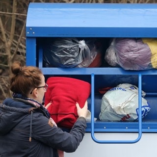 Frau wirft Kleidersäcke in Container