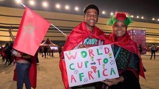 Zwei marokkanische Fans, ein junger Mann und eine Frau, halten ein Schild auf dem steht "World Cup to Africa"