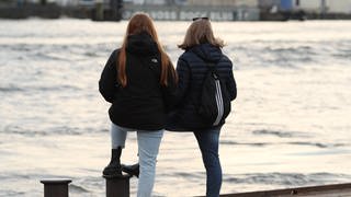 Freundinnen stehen an einer Hafenkante und schauen aufs Wasser