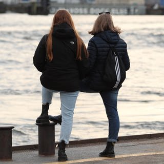 Freundinnen stehen an einer Hafenkante und schauen aufs Wasser