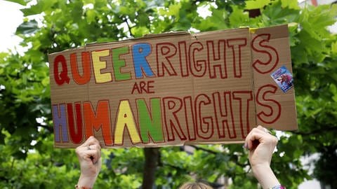 Eine Frau hält ein Plakat mit der Aufschrift "Queerrights are Humanrights" bei einer Demo hoch.