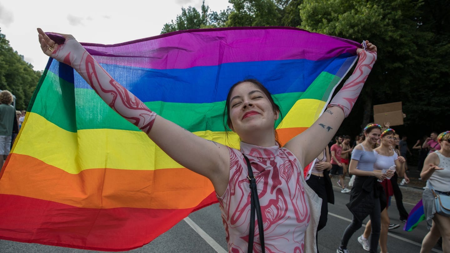 Eine lächelnde Frau hält stolz die Regenbogenflagge
